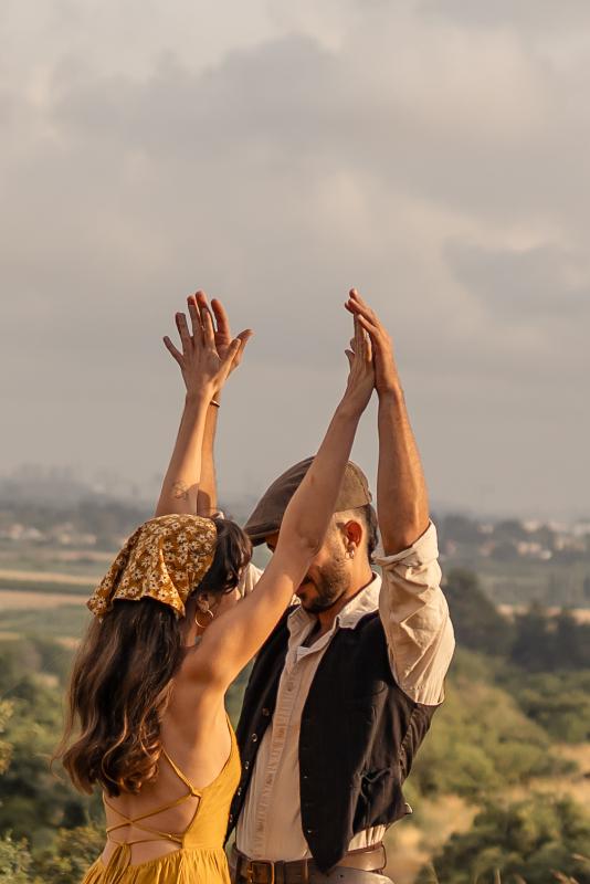 זוג מרים ידיים יחד מול נוף העמק — צילומי זוגיות בעמק יזרעאל