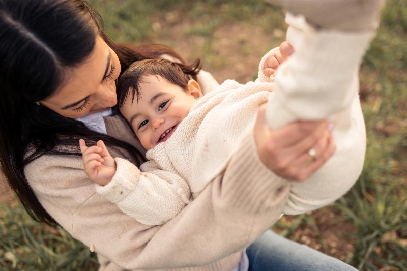 אמא מניפה תינוק צוחק בשדה – צילומי אמהות בטבע