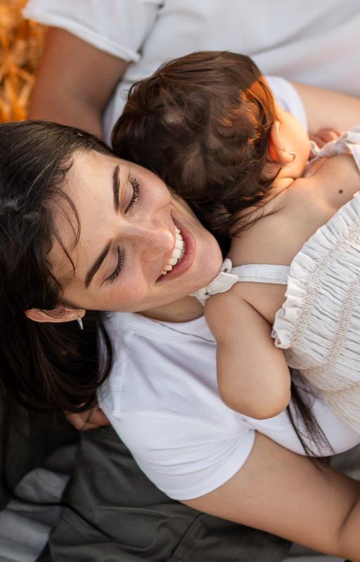 אמא מחבקת פעוטה מצולמת מלמעלה — צילומי גיל שנה ואמהות