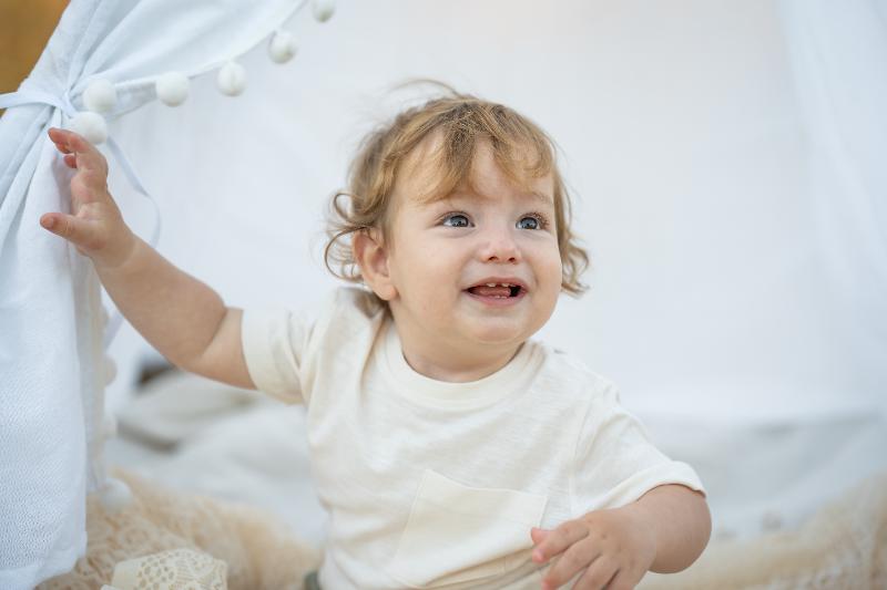 פעוט צוחק בפתח אוהל טיפי לבן — צילומי גיל שנה עם סט אביזרים