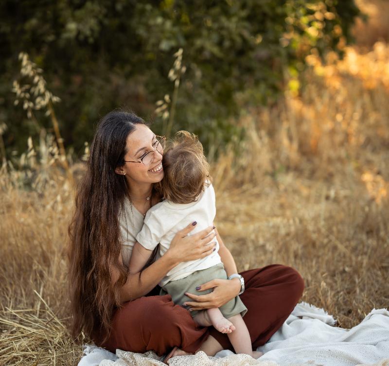 אמא מחבקת פעוט על שמיכה בשדה זהוב — צילומי גיל שנה ואמהות